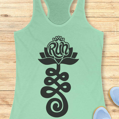A mint green racerback tank top with a black graphic of a lotus flower and infinity symbol containing the word 'Run', displayed flat on a light wood background with sneakers partially visible at the bottom right.