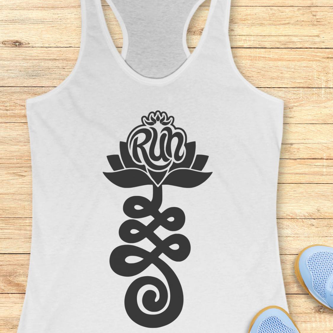A white racerback tank top with a black graphic of a lotus flower and the word 'Run' integrated into the petals, displayed flat on a light wood background with blue sneakers partially visible at the bottom right.