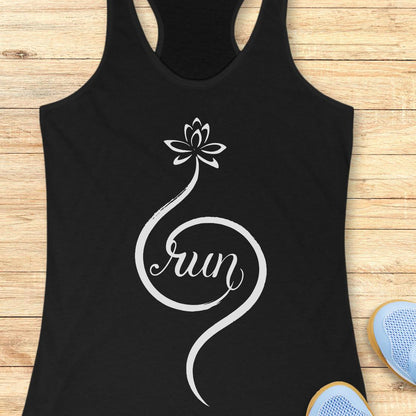 A black racerback tank top laid flat on a light wood surface, featuring a white graphic of a lotus flower and the word 'run' in script. Part of a blue shoe is visible at the bottom right as a styling prop.
