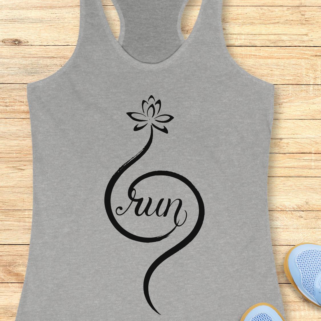 A heather gray racerback tank top with a black graphic of a lotus flower and the word 'run' in script, laid flat on a light wood background with partial blue sneakers visible at the edges.