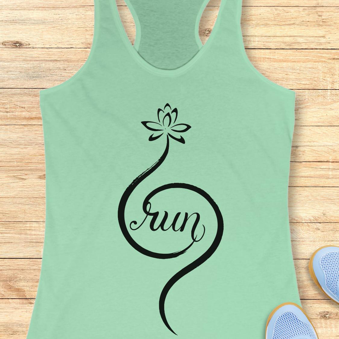 A mint green racerback tank top with a black graphic of a lotus flower and the word 'run' in script, laid flat on a light wood background with partial sneakers visible at the edges.