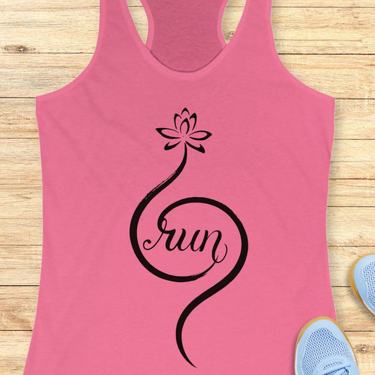 A pink racerback tank top with a black graphic of a lotus flower and the word 'run' in script, laid flat on a light wood background with partial blue sneakers visible at the edges.