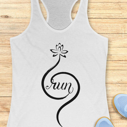 A white racerback tank top with a black lotus flower and the word 'Run' in script, laid flat on a light wood background with partial blue sneakers visible at the bottom right.