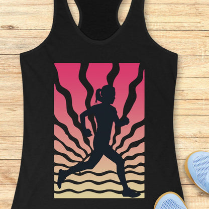A black racerback tank top laid flat on a light wood surface, featuring a large graphic print of a running silhouette against a pink-to-beige gradient with wavy lines. Part of a blue shoe is visible at the bottom right.