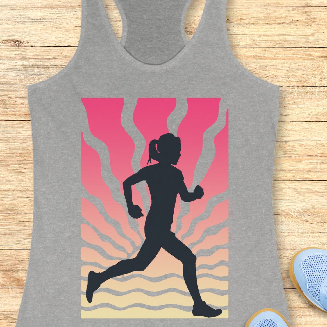 A heather gray racerback tank top featuring a graphic print of a black runner silhouette against a pink, orange, and beige wavy background, displayed flat on a light wood surface.
