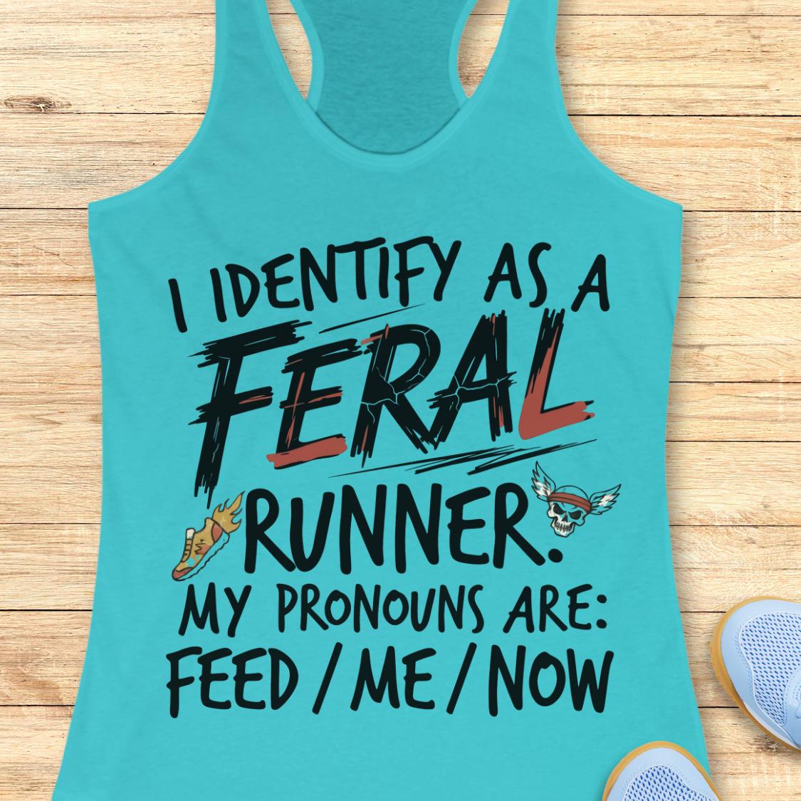 A turquoise racerback tank top laid flat on a light wood surface, printed with the phrase 'I IDENTIFY AS A FERAL RUNNER. MY PRONOUNS ARE: FEED / ME / NOW' in black lettering with red and orange accents, plus small graphic illustrations.