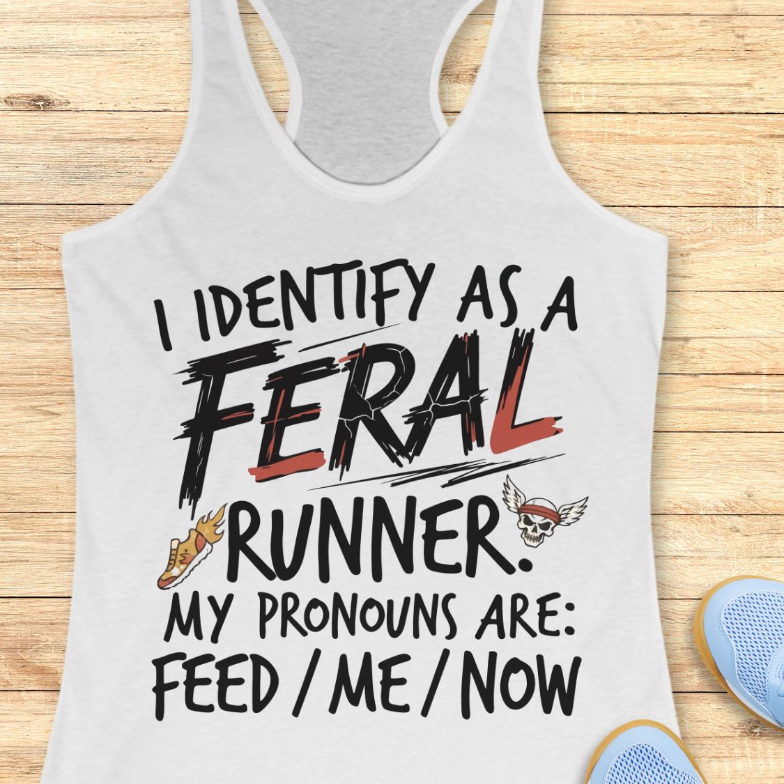 A white racerback tank top laid flat on a light wood background, featuring a graphic print that reads 'I IDENTIFY AS A FERAL RUNNER. MY PRONOUNS ARE: FEED / ME / NOW' with a shoe and skull-and-wing illustration.