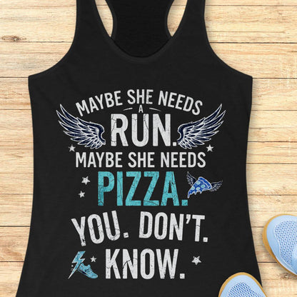 A black racerback tank top laid flat on a light wood background, featuring a humorous graphic print that reads 'MAYBE SHE NEEDS A RUN. MAYBE SHE NEEDS PIZZA.