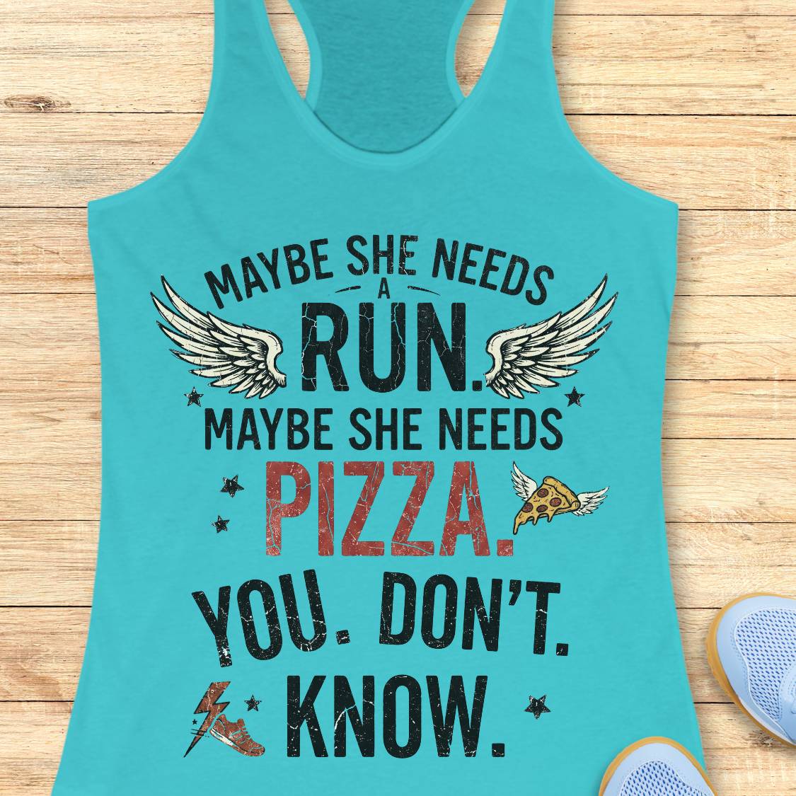 A turquoise racerback tank top laid flat on a light wood surface, featuring a distressed graphic that reads 'MAYBE SHE NEEDS A RUN. MAYBE SHE NEEDS PIZZA.