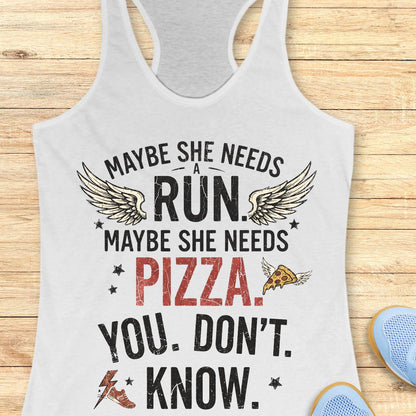 A white racerback tank top laid flat on a light wood background, printed with the phrase “MAYBE SHE NEEDS A RUN. MAYBE SHE NEEDS PIZZA.
