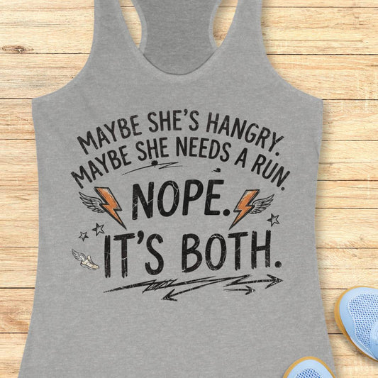 A heather gray racerback tank top with a humorous graphic printed on the front, laid flat on a light wood plank background. The graphic reads 'MAYBE SHE'S HANGRY.