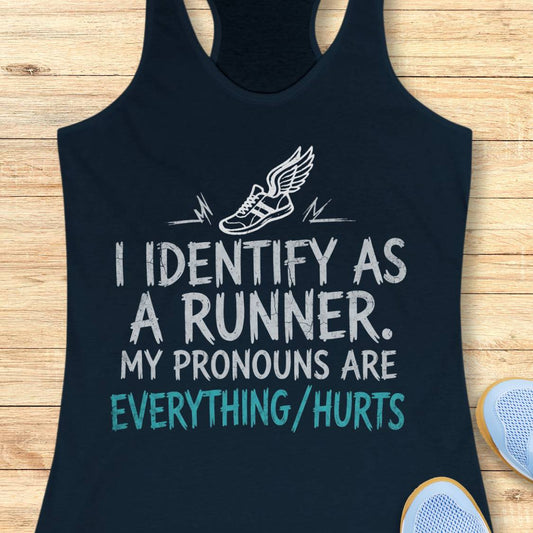 A navy racerback tank top laid flat on a light wood background, featuring a white winged running shoe graphic and the text 'I IDENTIFY AS A RUNNER. MY PRONOUNS ARE EVERYTHING/HURTS' in white and teal.