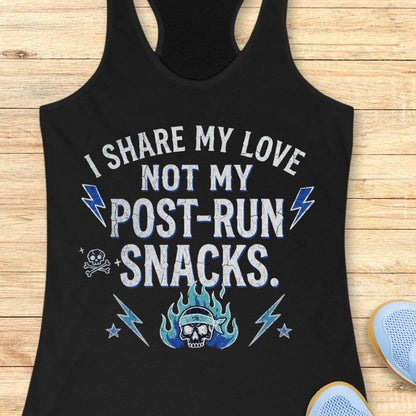 A black racerback tank top laid flat on a light wood surface, featuring a distressed graphic that reads 'I SHARE MY LOVE NOT MY POST-RUN SNACKS.' in white and blue, with lightning bolts, stars, a skull, and flames.