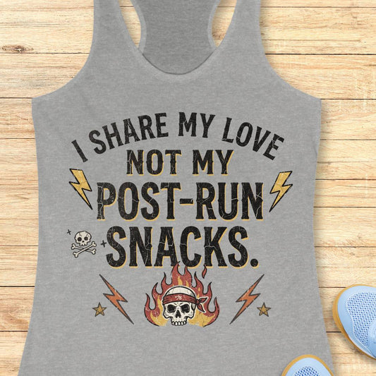 A heather gray racerback tank top laid flat on a light wood background, featuring a distressed graphic that reads 'I SHARE MY LOVE NOT MY POST-RUN SNACKS.' with lightning bolts, a skull, and flames.