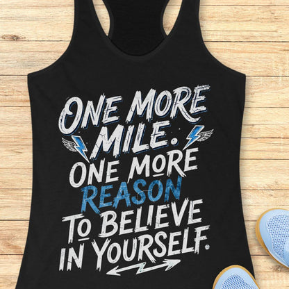 A black racerback tank top featuring  the text 'one more mile. one more reason to believe in yourself' printed on the front, displayed flat on a light wood background.