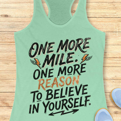 A mint racerback tank top featuring  the text 'one more mile. one more reason to believe in yourself' printed on the front, displayed flat on a light wood background.