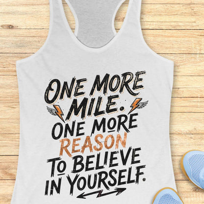A white racerback tank top featuring  the text 'one more mile. one more reason to believe in yourself' printed on the front, displayed flat on a light wood background.