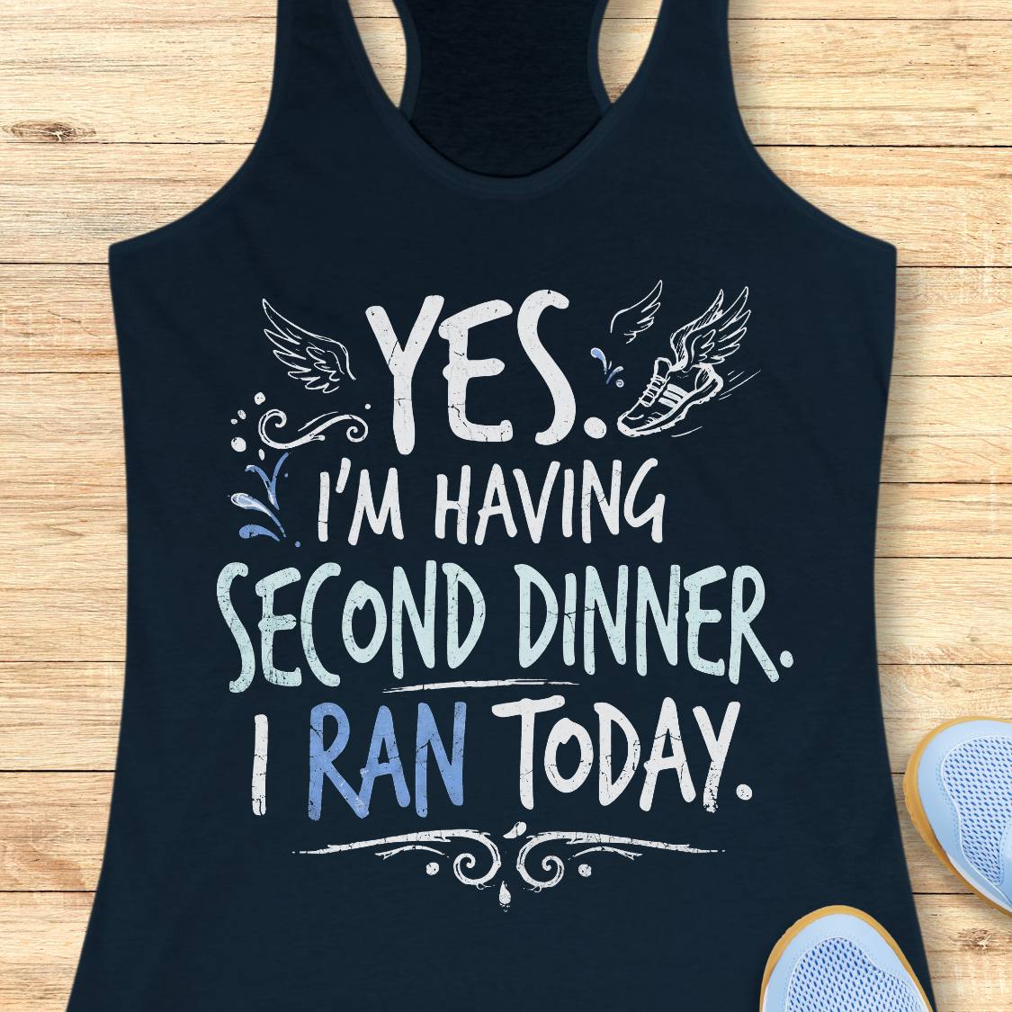 A  navy racerback tank top featuring  the text 'yes. I'm having second dinner. I ran today.' printed on the front, displayed flat on a light wood background.