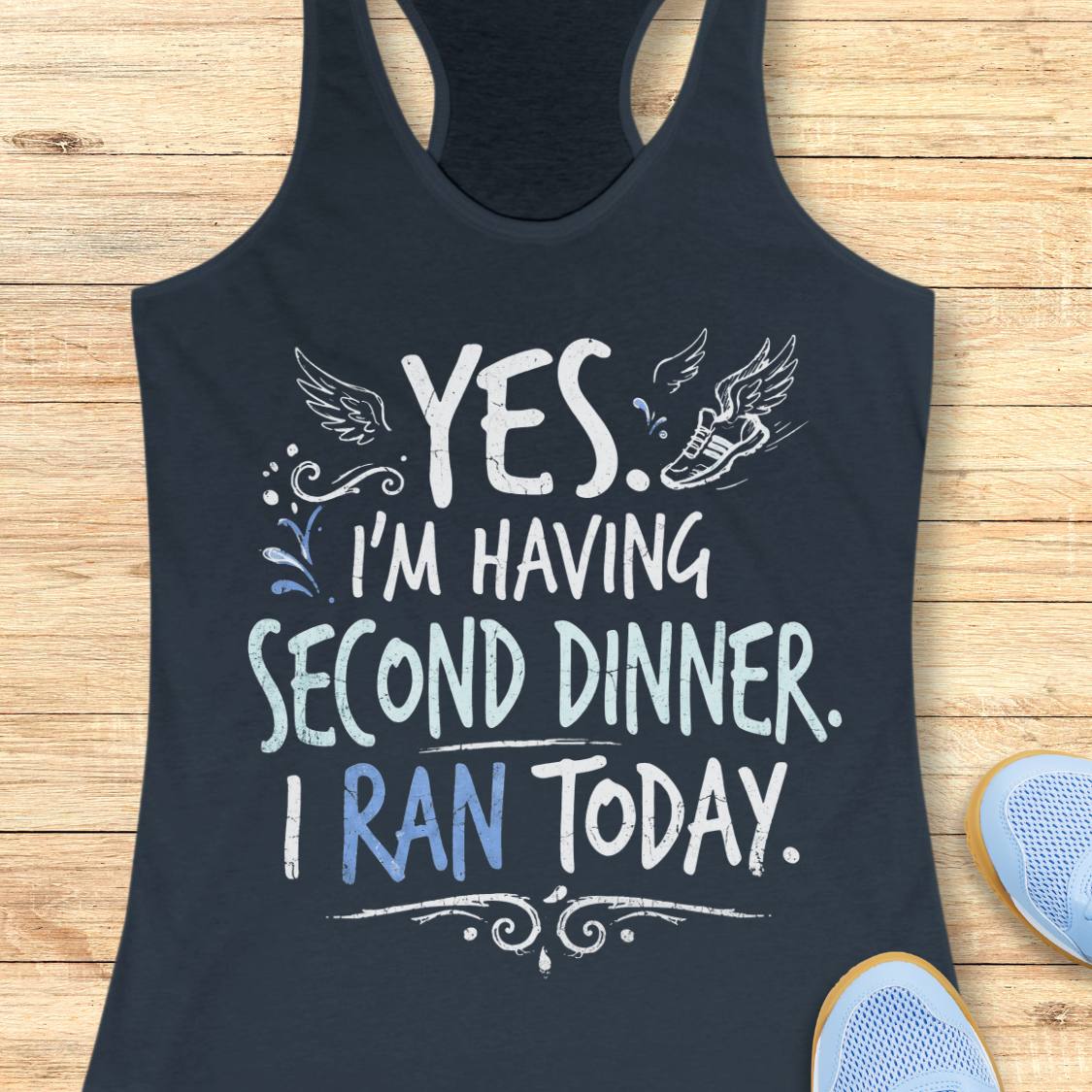 A indigo racerback tank top featuring  the text 'yes. I'm having second dinner. I ran today.' printed on the front, displayed flat on a light wood background.