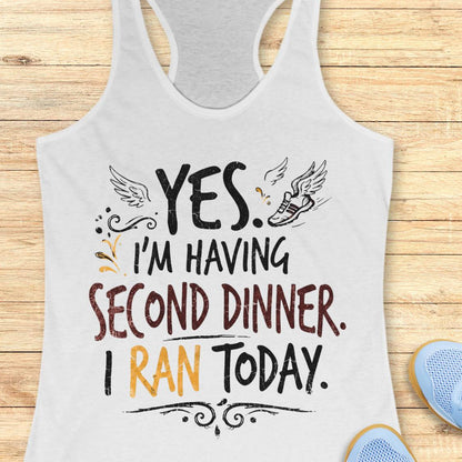 A white racerback tank top featuring  the text 'yes. I'm having second dinner. I ran today.' printed on the front, displayed flat on a light wood background.