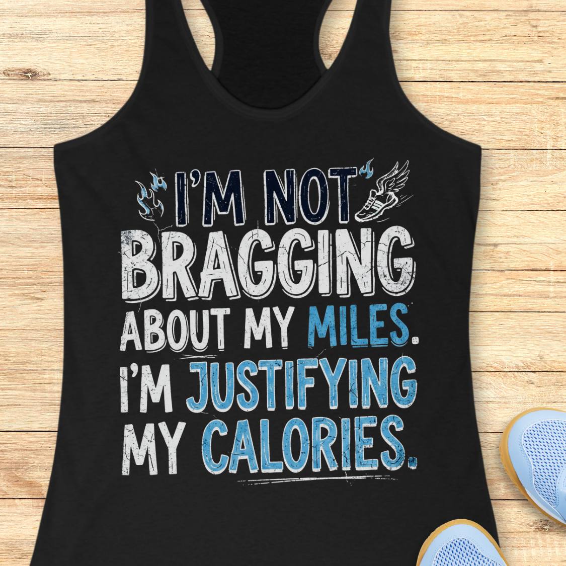 A  black racerback tank top featuring  the text 'I'm not bragging about my miles. I'm justifying my calories' printed on the front, displayed flat on a light wood background.