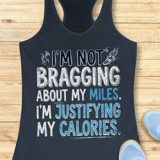 A  indigo racerback tank top featuring  the text 'I'm not bragging about my miles. I'm justifying my calories' printed on the front, displayed flat on a light wood background.