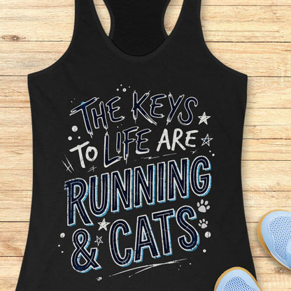 A black racerback tank top laid flat on a light wood surface, featuring the phrase 'THE KEYS TO LIFE ARE RUNNING & CATS' in white and blue outlined lettering with small paw print and star accents. Part of a light blue shoe is visible at the bottom right.