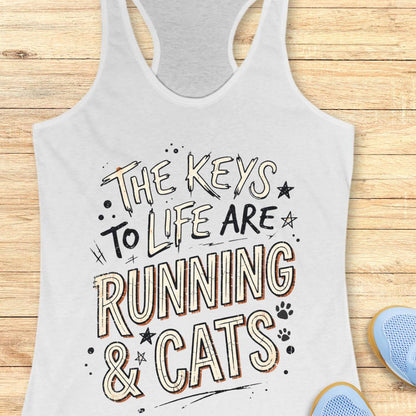 A white racerback tank top with a graphic print that reads 'THE KEYS TO LIFE ARE RUNNING & CATS' in stylized lettering, shown laid flat on a light wood background with partial blue sneakers visible at the edges.