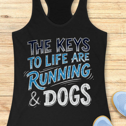 A black racerback tank top laid flat on a light wood background, featuring the text 'THE KEYS TO LIFE ARE RUNNING & DOGS' in white and blue distressed lettering. Partial blue sneakers are visible at the bottom right as styling props.