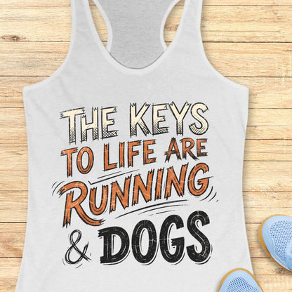 A white racerback tank top laid flat on a light wood background, printed with the phrase 'THE KEYS TO LIFE ARE RUNNING & DOGS' in stylized beige, orange, and black lettering. Part of a blue shoe is visible at the bottom right as a styling prop.