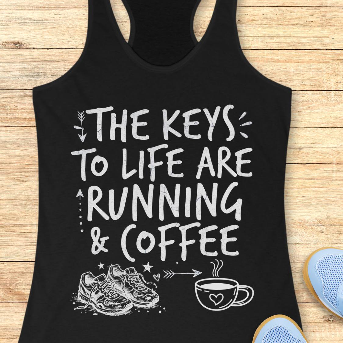 A black racerback tank top with a white graphic print that reads 'THE KEYS TO LIFE ARE RUNNING & COFFEE' with sneakers and a coffee cup illustration, shown laid flat on a light wood background with partial blue shoes visible at the edges.