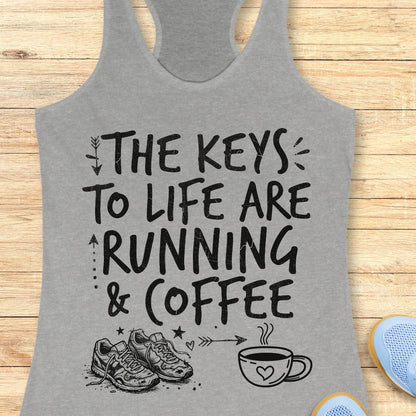 A heather gray racerback tank top with a black graphic print that reads 'THE KEYS TO LIFE ARE RUNNING & COFFEE' with running shoes and a coffee cup illustration, shown on a light wood background.