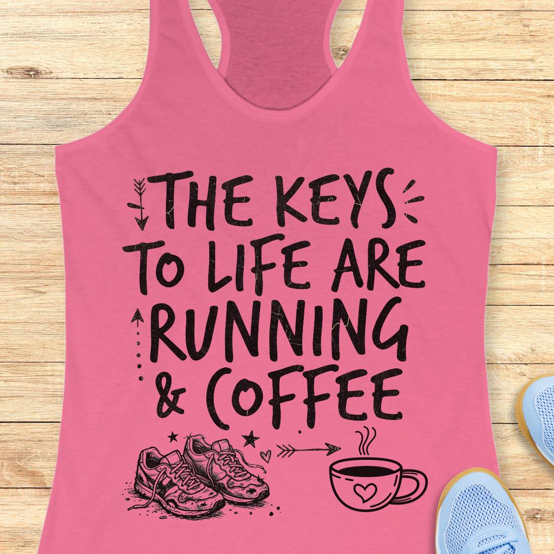 A pink racerback tank top with a black graphic print reading 'THE KEYS TO LIFE ARE RUNNING & COFFEE' with sneakers and a coffee cup illustration, shown on a light wood plank background with partial blue shoes at the edges.