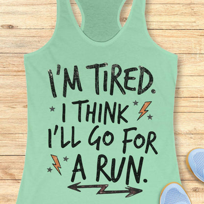 A mint green racerback tank top laid flat on a light wood background, featuring the text 'I'M TIRED. I THINK I'LL GO FOR A RUN.