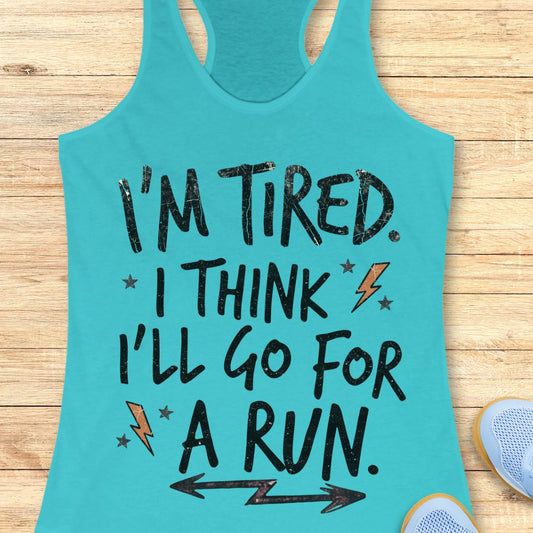 A turquoise racerback tank top laid flat on a light wood surface, with black distressed text reading “I'M TIRED. I THINK I'LL GO FOR A RUN.