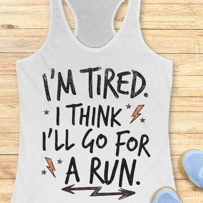 A white racerback tank top with a humorous motivational graphic that reads 'I'M TIRED. I THINK I'LL GO FOR A RUN.