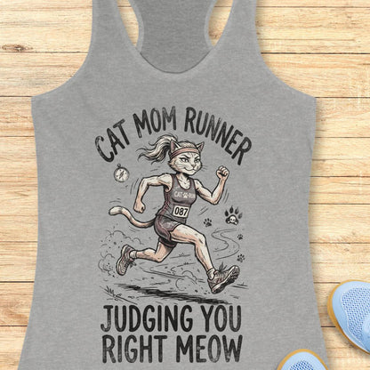 A heather gray racerback tank top laid flat on a light wood background, featuring a graphic of a cat dressed as a race runner with the text 'CAT MOM RUNNER' above and 'JUDGING YOU RIGHT MEOW' below.