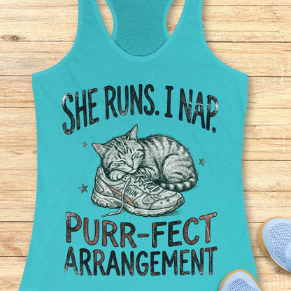 A turquoise racerback tank top laid flat on a light wood surface, featuring a graphic of a sleeping cat curled up inside a sneaker with the text 'SHE RUNS. I NAP.