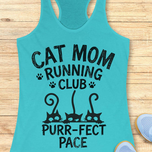 A turquoise racerback tank top laid flat on a light wood surface, printed with the phrase 'CAT MOM RUNNING CLUB PURR-FECT PACE' in black lettering with paw prints and cat silhouettes. Part of a light blue shoe is visible at the bottom right.