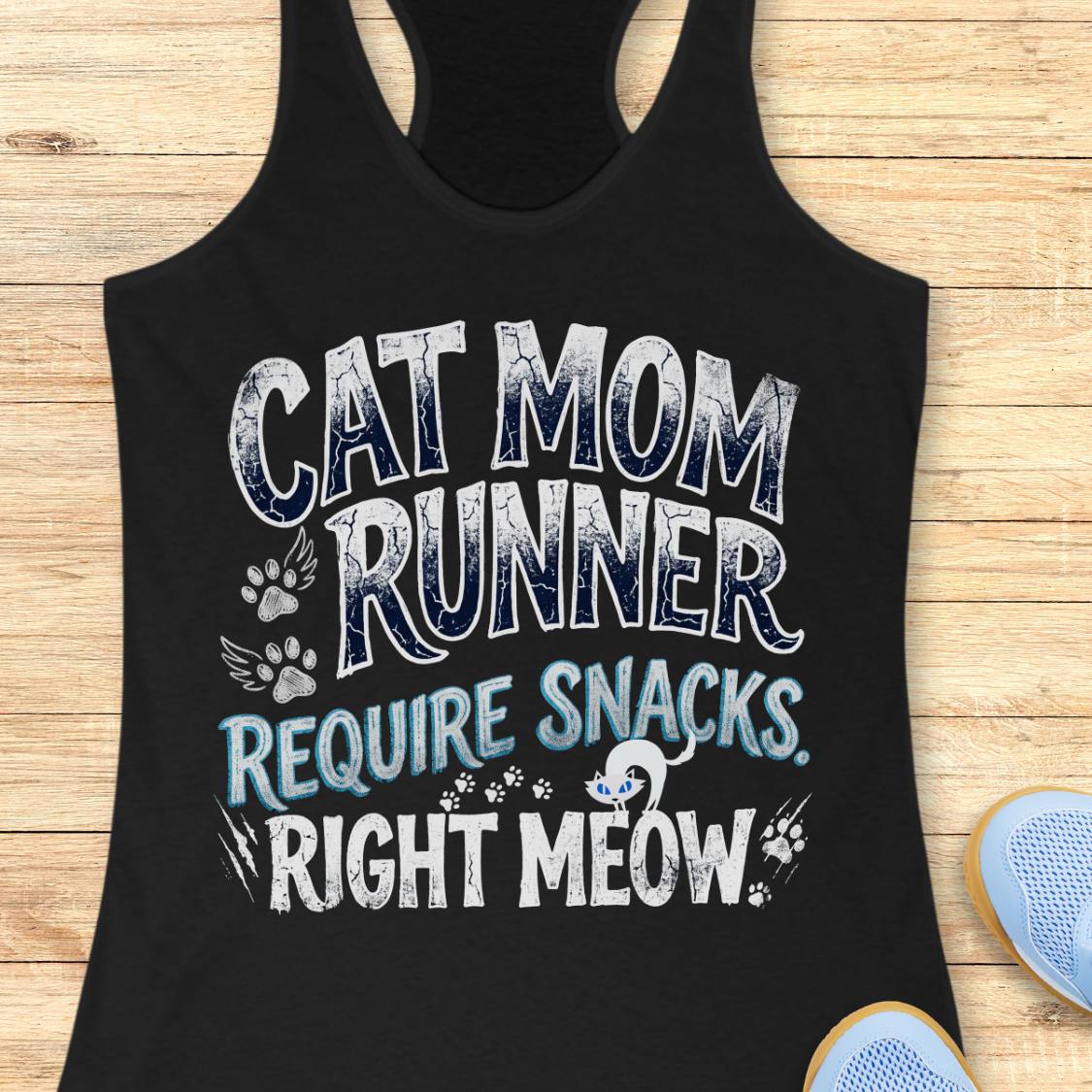 A black racerback tank top laid flat on a light wood background, featuring the text 'CAT MOM RUNNER REQUIRE SNACKS. RIGHT MEOW.