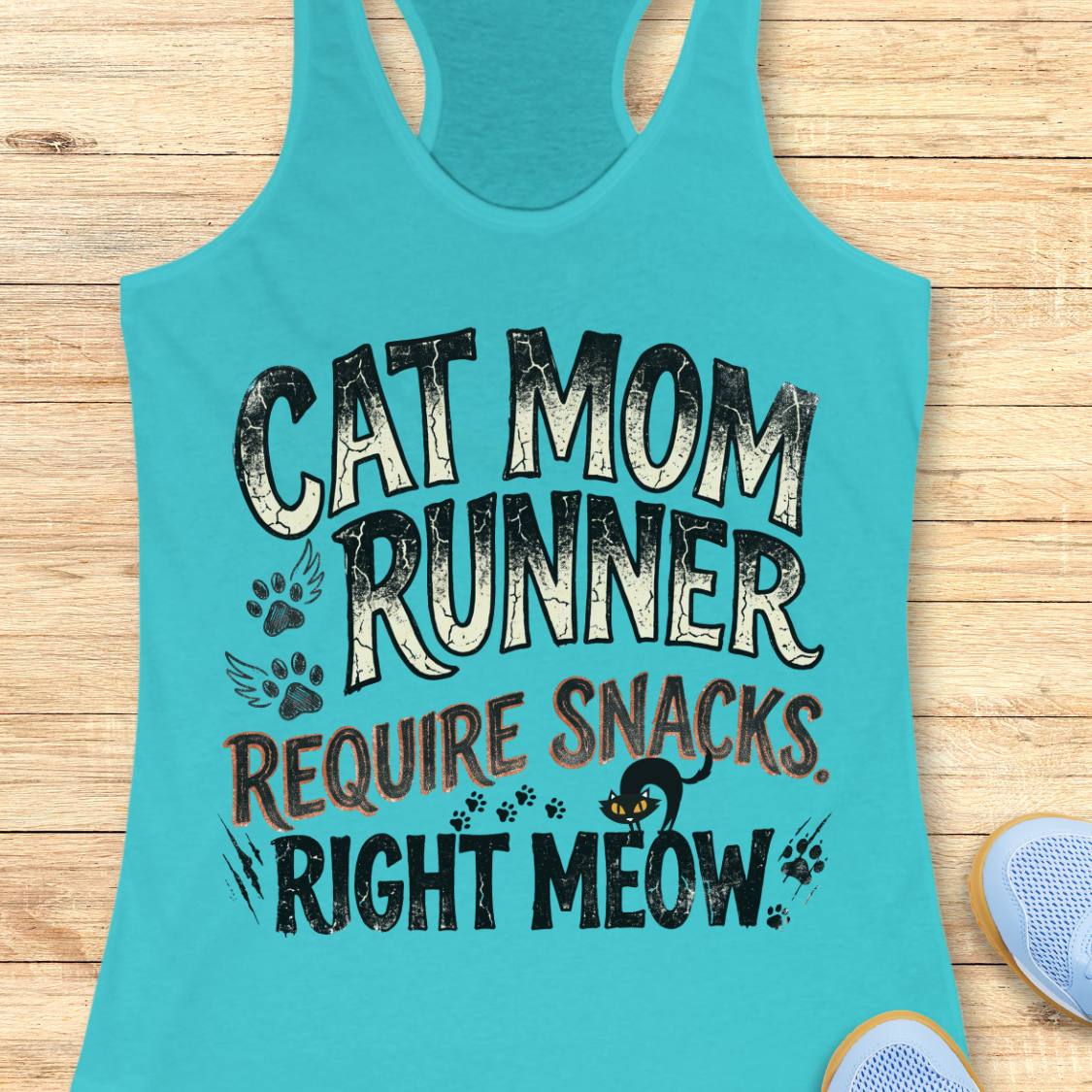 A turquoise racerback tank top laid flat on a light wood surface, featuring the text 'CAT MOM RUNNER REQUIRE SNACKS RIGHT MEOW' with paw prints and a small cat graphic. Part of a light blue shoe is visible at the bottom right.