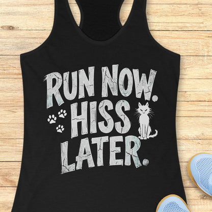 A black racerback tank top laid flat on a light wood surface, featuring the phrase 'RUN NOW. HISS LATER.