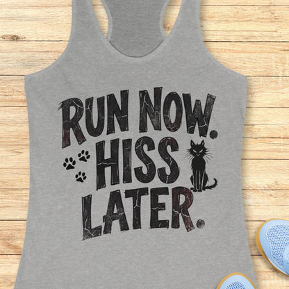 A heather gray racerback tank top laid flat on a light wood surface, featuring the phrase 'RUN NOW. HISS LATER.