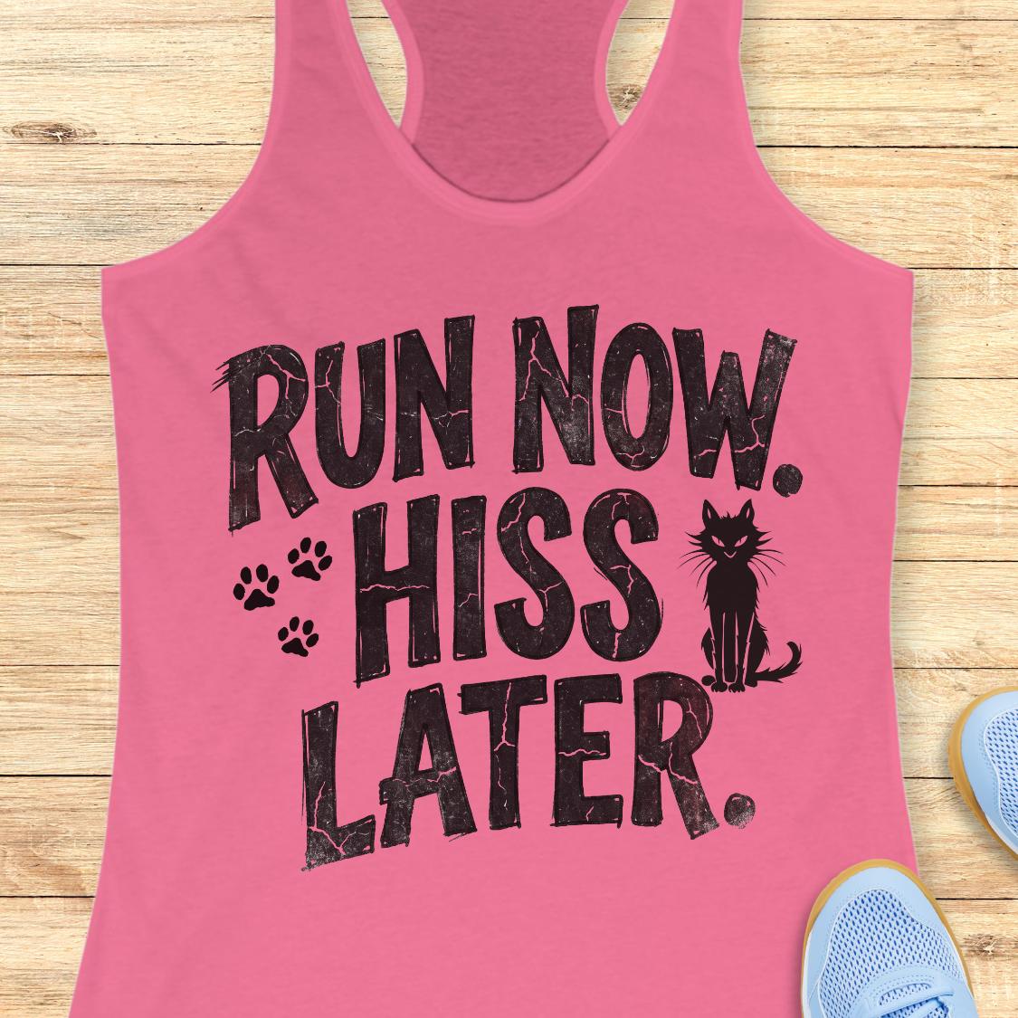 A pink racerback tank top laid flat on a light wood surface, featuring the bold black text 'RUN NOW. HISS LATER.