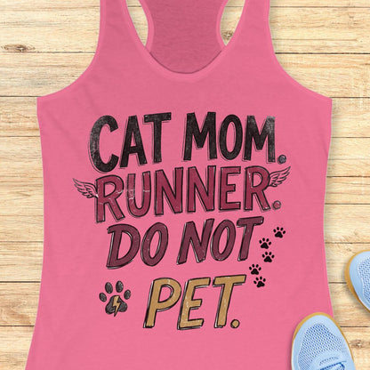 A pink racerback tank top laid flat on a light wood surface, featuring the text 'CAT MOM. RUNNER.