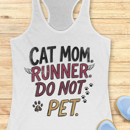 A white racerback tank top laid flat on a light wood background, featuring the text 'CAT MOM. RUNNER.