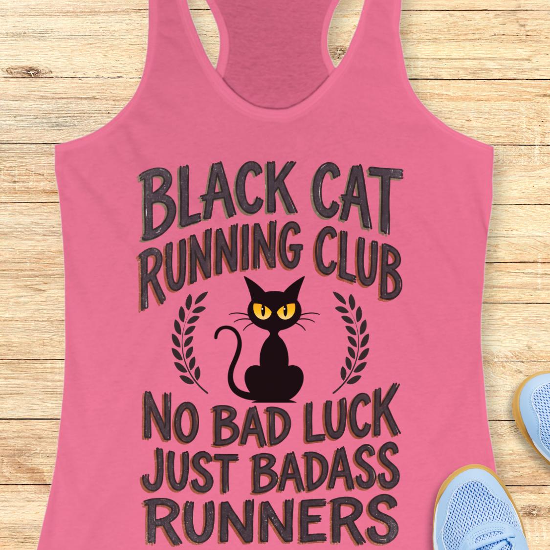 A pink racerback tank top laid flat on a light wood surface, featuring a black cat graphic with yellow eyes and the text 'BLACK CAT RUNNING CLUB' and 'NO BAD LUCK JUST BADASS RUNNERS.' Partial blue sneakers are visible at the edges as styling props.