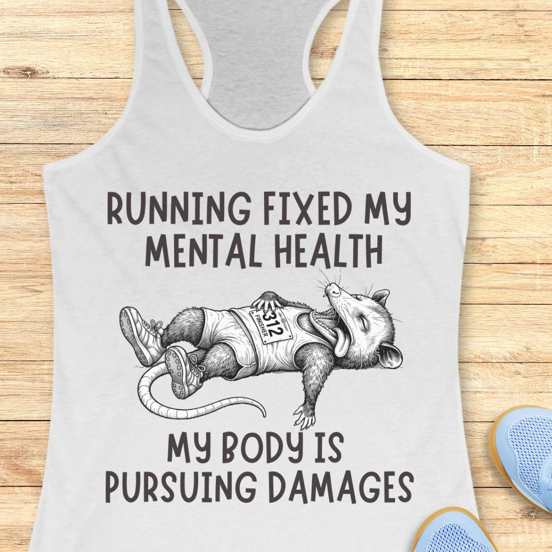 A white racerback tank top laid flat on a light wood surface, featuring a black graphic of a cartoon opossum wearing a race bib and the text 'RUNNING FIXED MY MENTAL HEALTH' and 'MY BODY IS PURSUEING DAMAGES'. Partial blue shoes are visible at the bottom right as styling props.