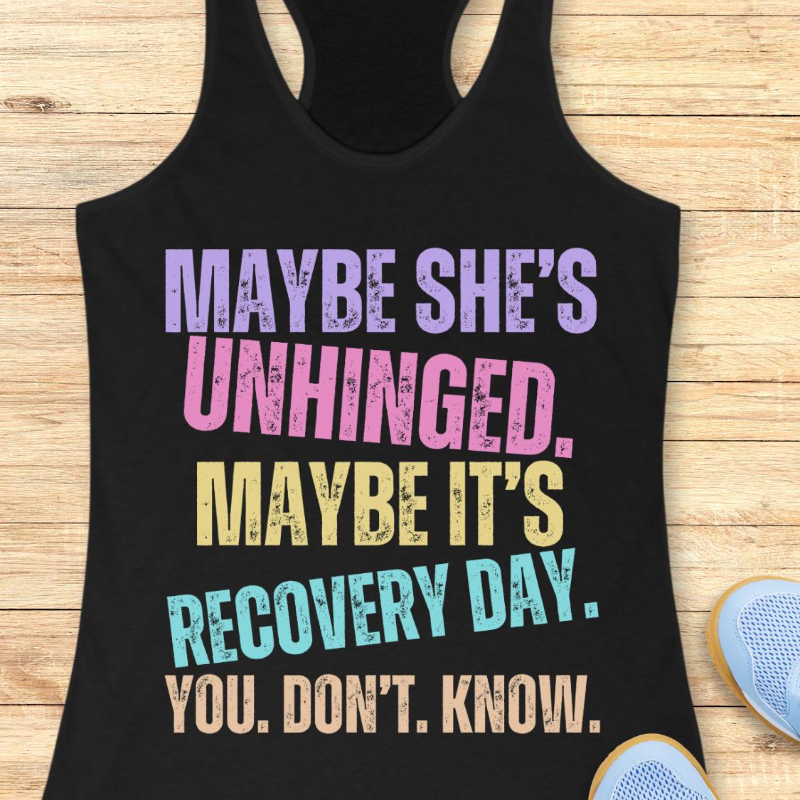 A black racerback tank top with a colorful distressed text graphic reading 'MAYBE SHE'S UNHINGED. MAYBE IT'S RECOVERY DAY.