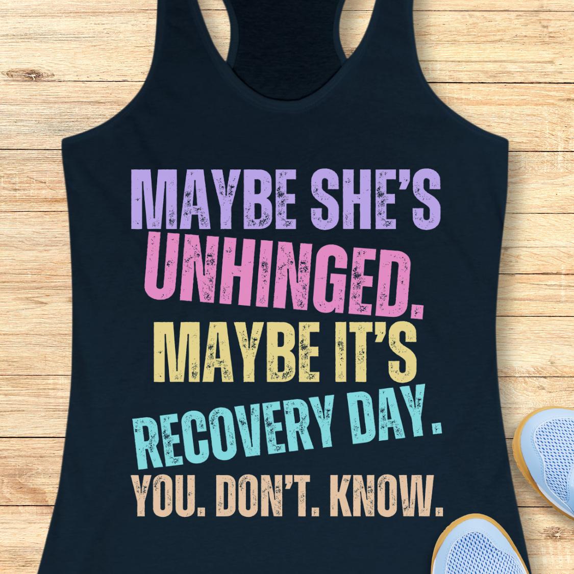 A navy racerback tank top with a colorful distressed text graphic reading 'MAYBE SHE'S UNHINGED. MAYBE IT'S RECOVERY DAY.